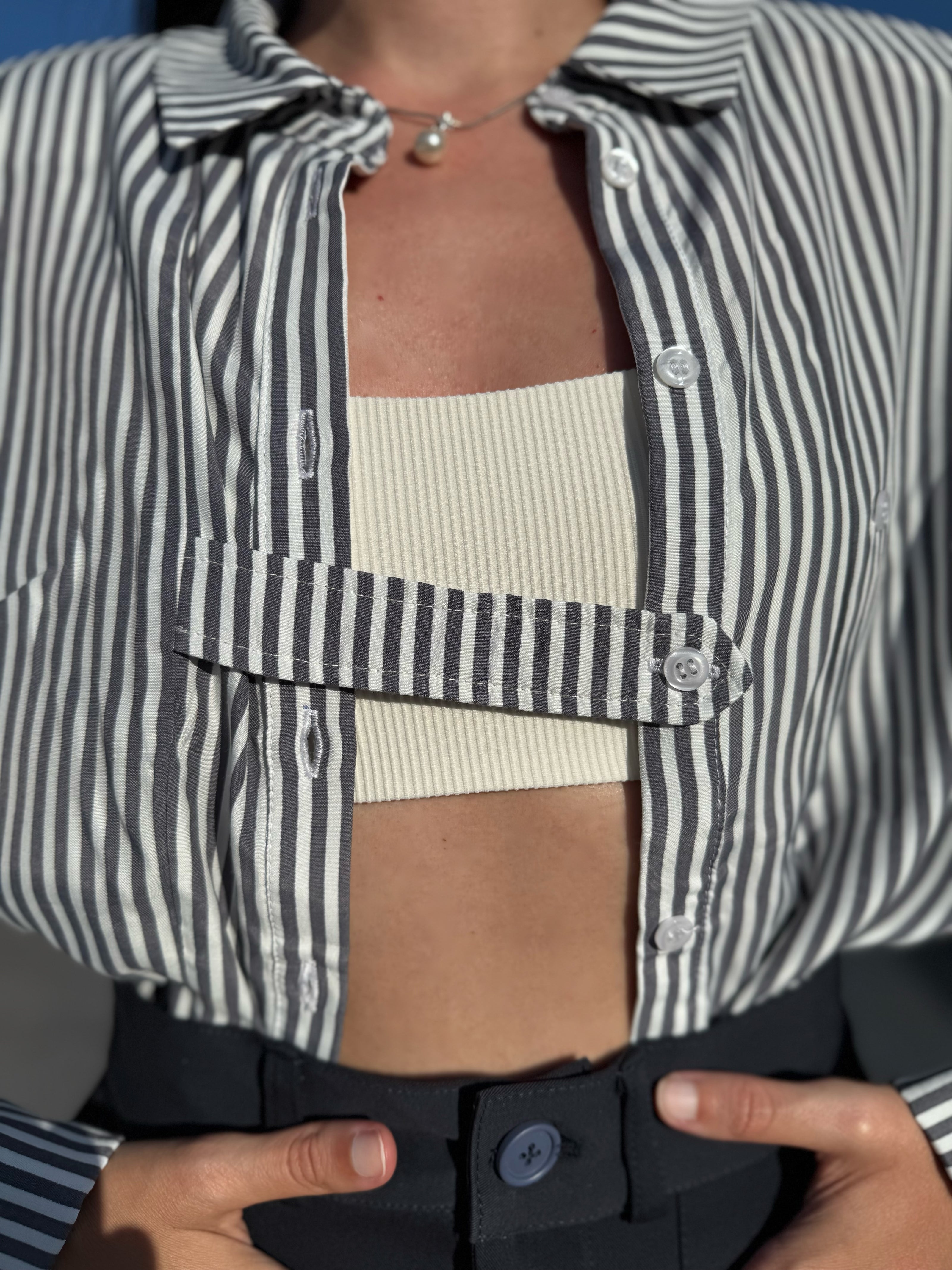 Person wearing a striped shirt over a ribbed top with a blurred background