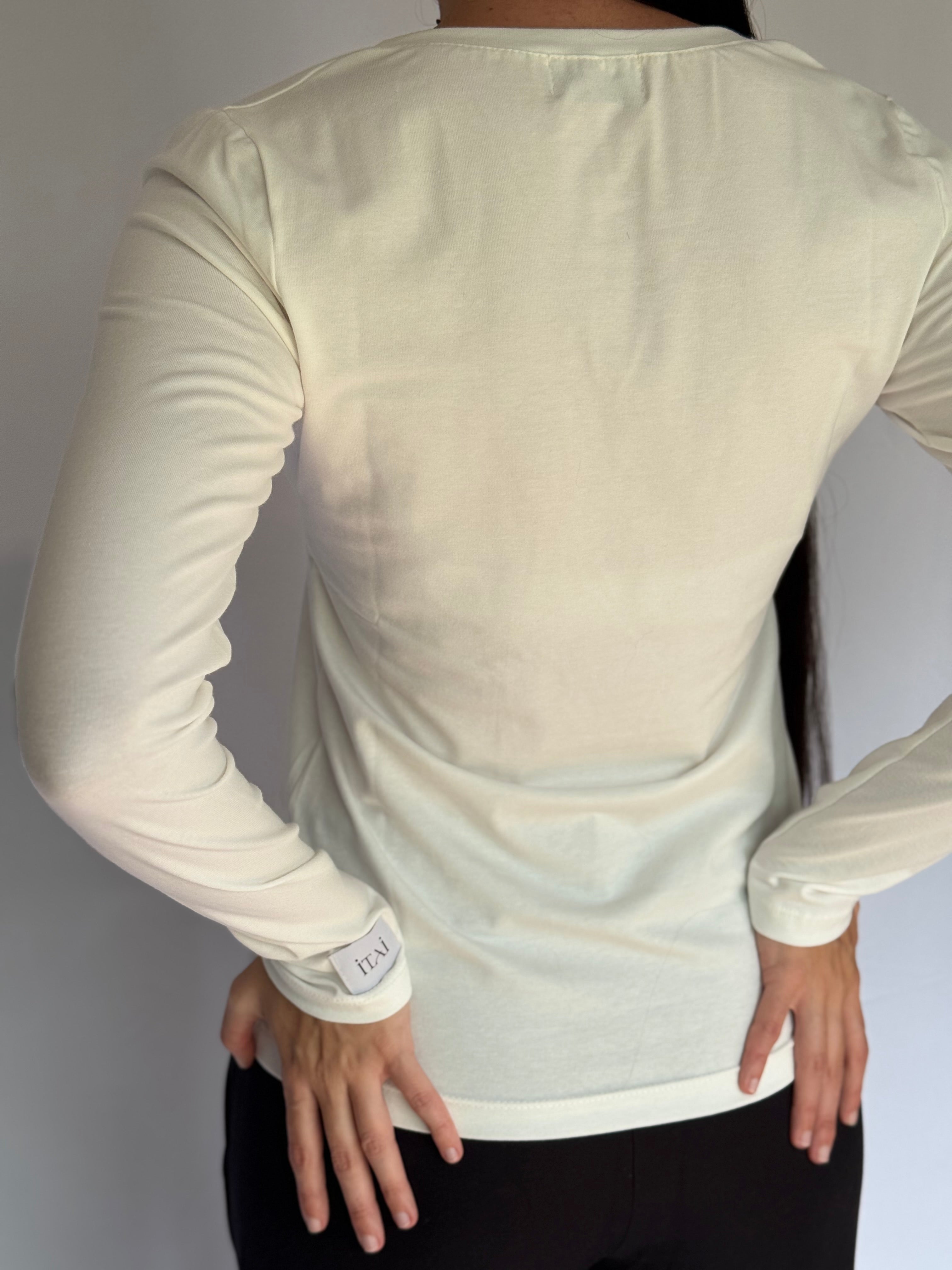 The back picture of a young woman wearing a light-colored long-sleeve shirt with a visible ITAI brand logo on a plain background