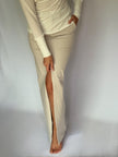 A woman wearing a long beige skirt with a slit on a plain background