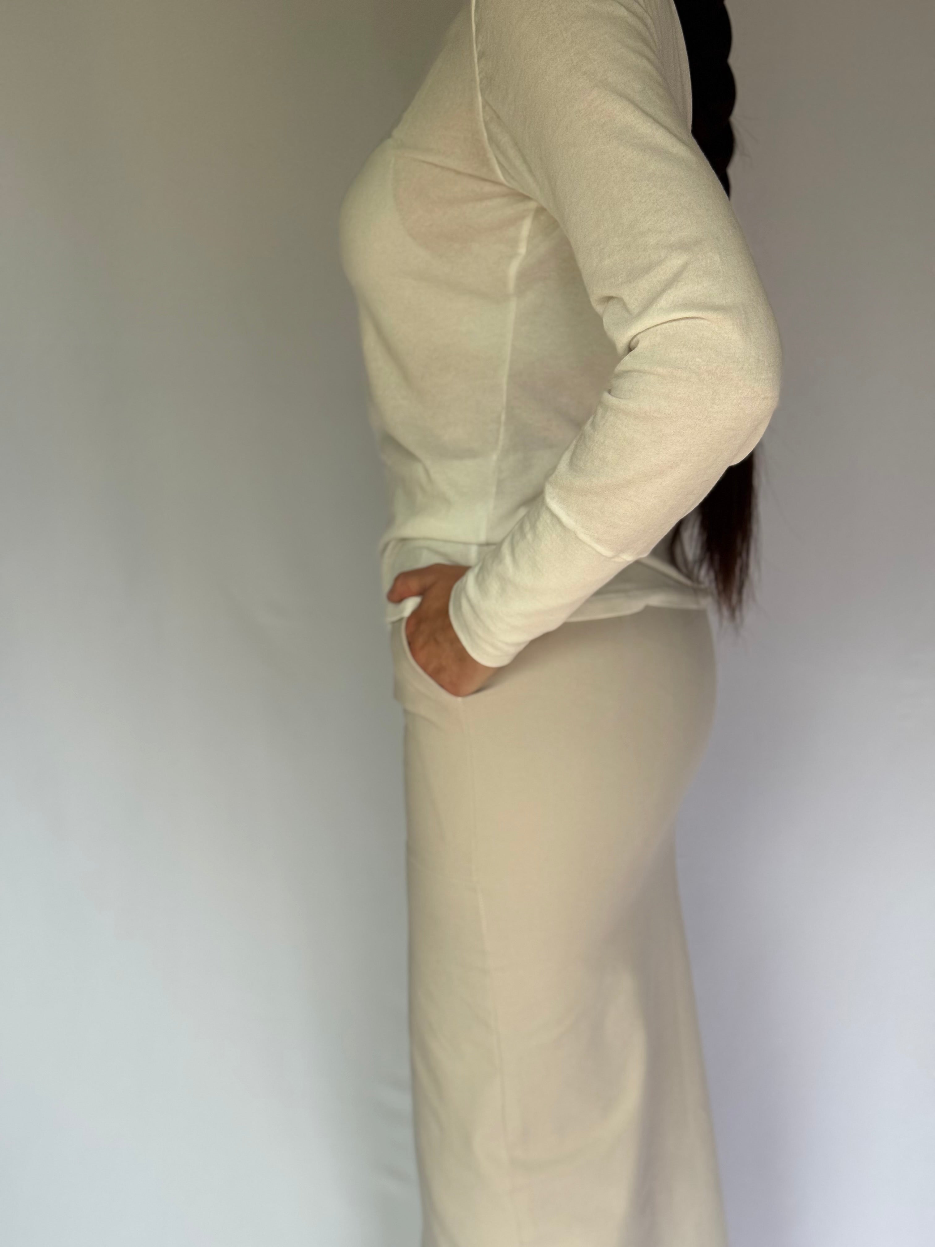 A young woman wearing a beige long-sleeve top and pants against a plain background