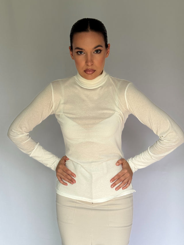A beautiful model wearing a white turtleneck see through shirt against a plain background