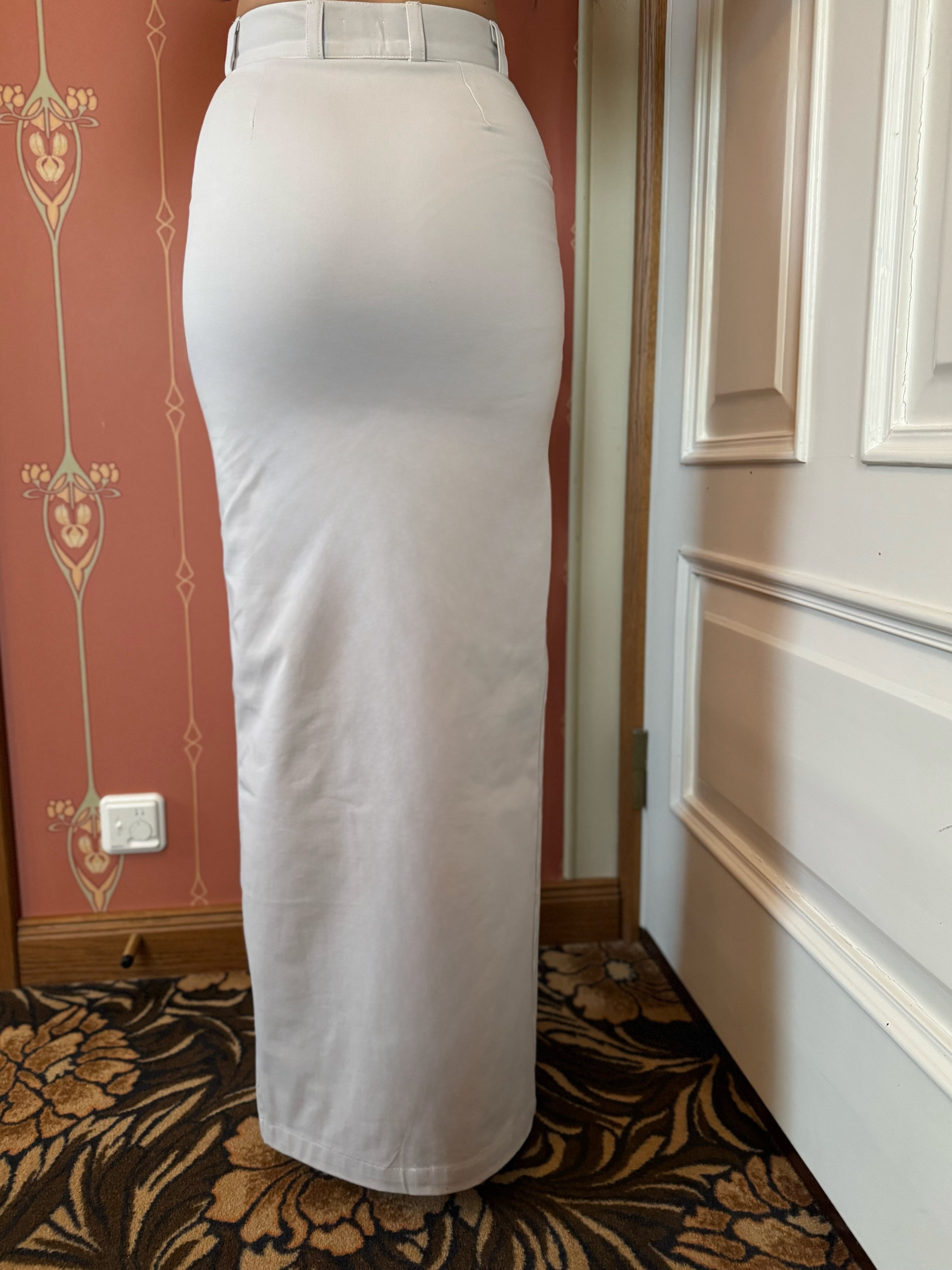 White skirt worn by a person in a room with decorative wallpaper and a door.