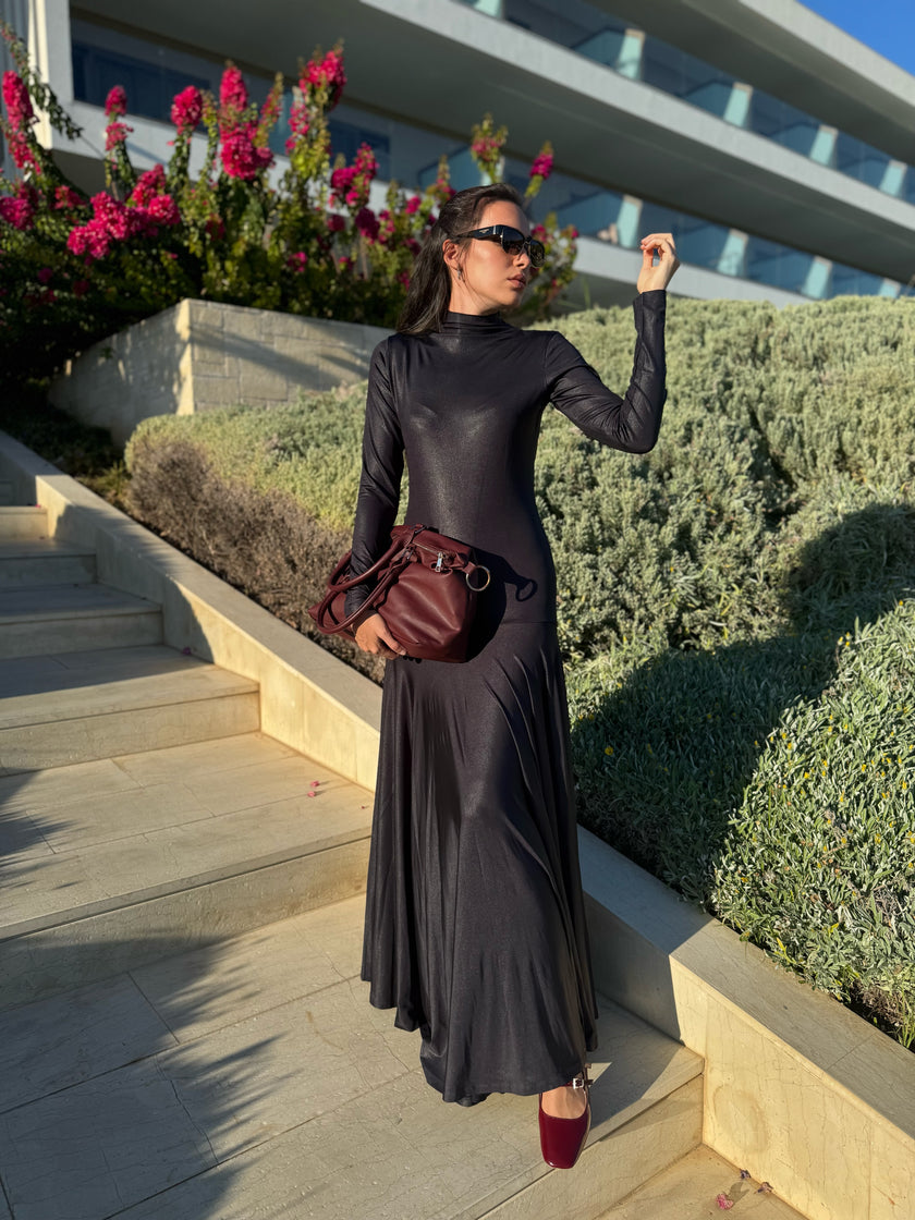 Woman in a long black dress standing outdoors with flowers and a building in the background. She is ready for a party in Ibiza!