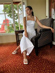 Woman in a white dress sitting on a chair in a room with a red patterned carpet and a window view.