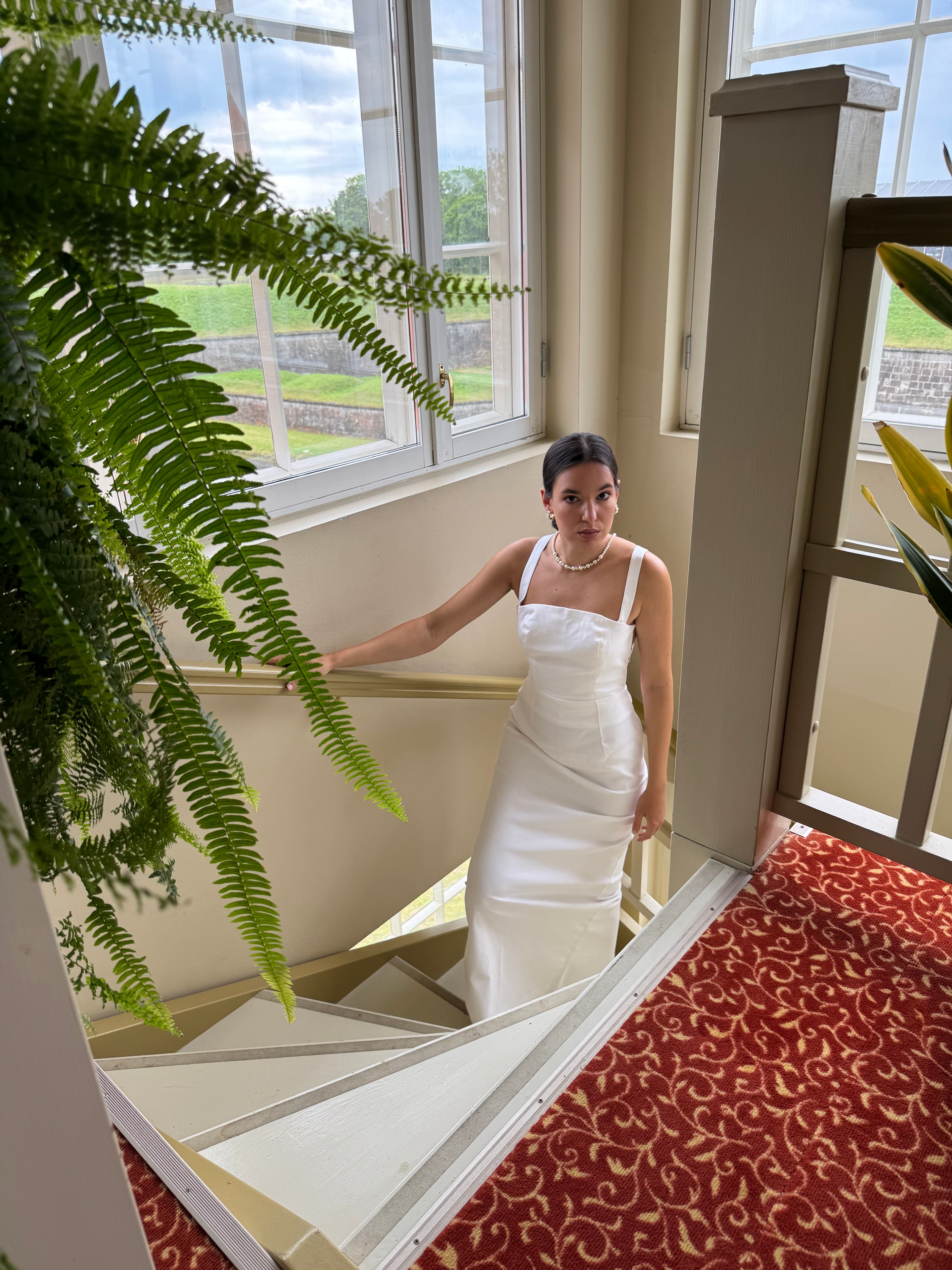 Woman in a white dress standing in a room with large windows and a patterned rug.