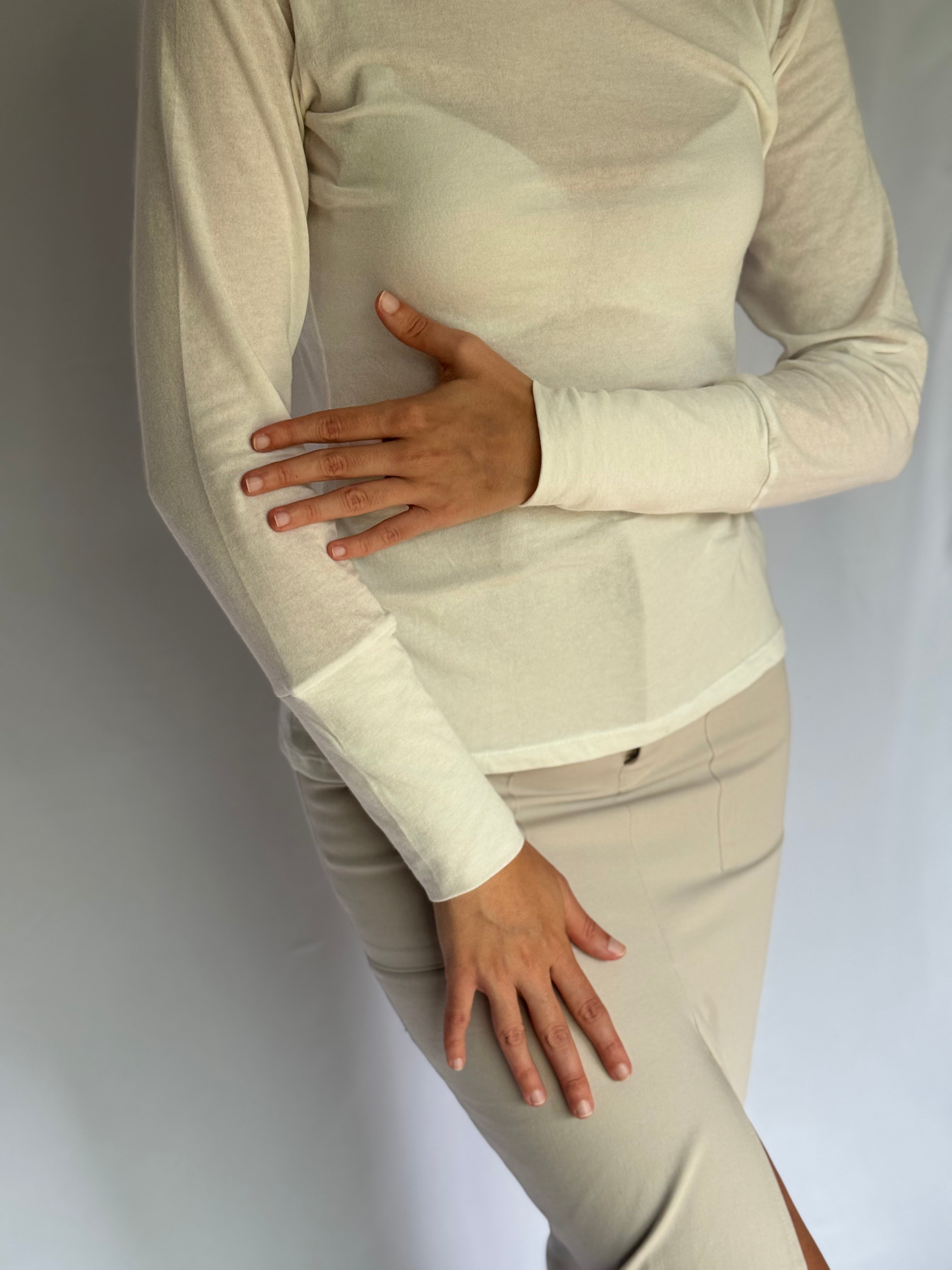 A young woman wearing an ivory see through long-sleeve top and skirt against a plain background
