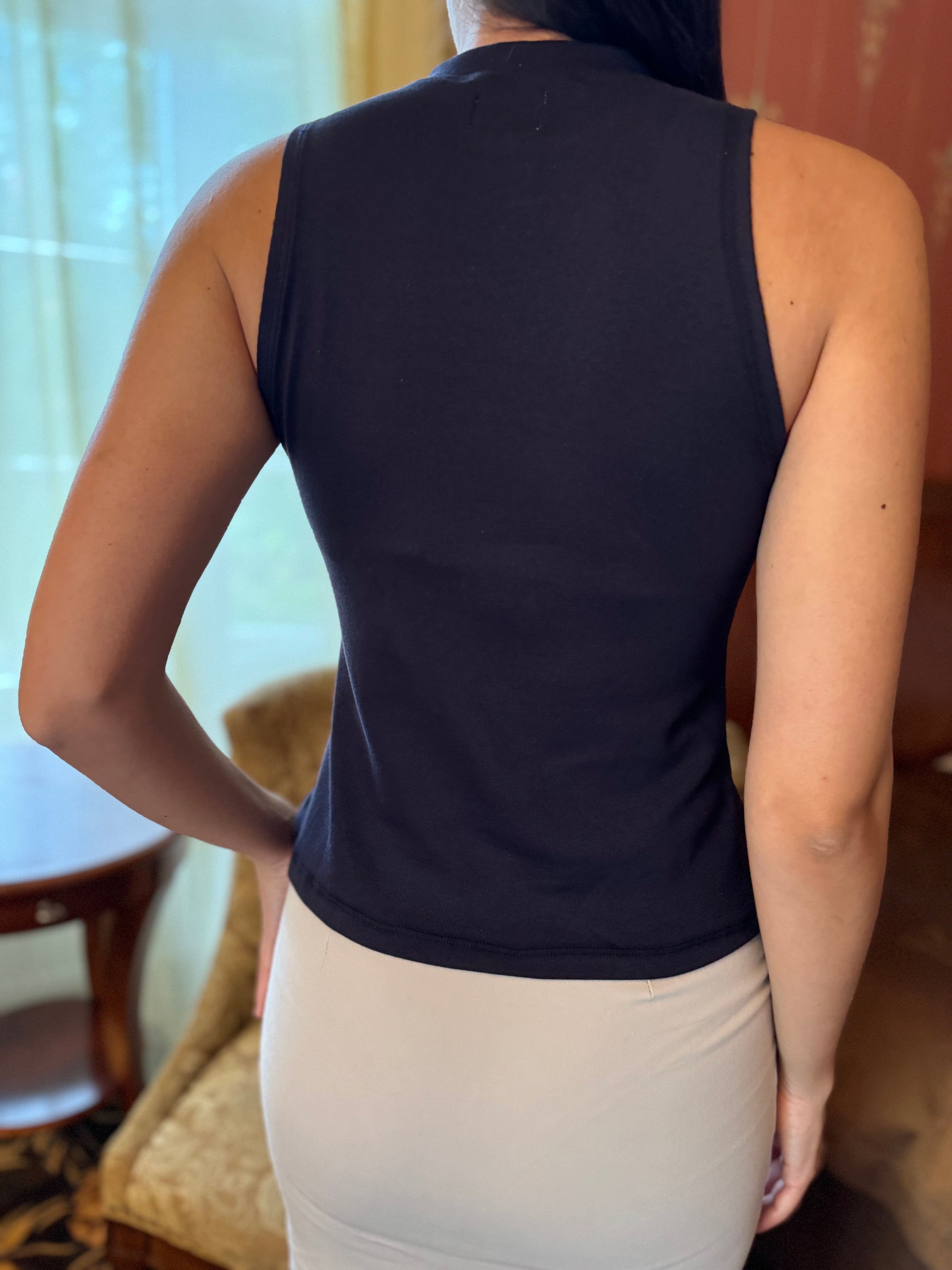 Person wearing a navy blue sleeveless top and beige pants in an indoor setting.
