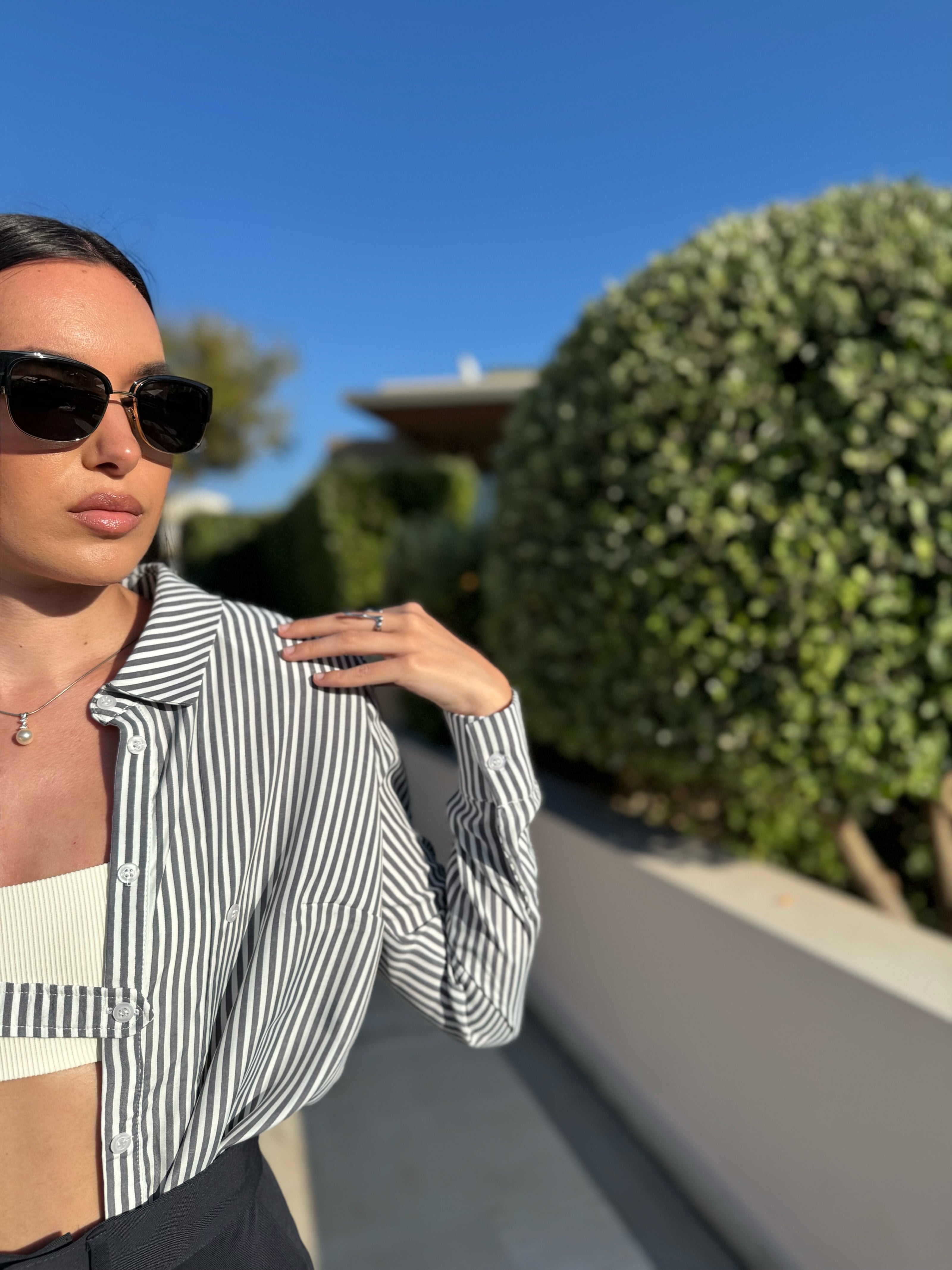 Woman wearing a striped shirt and sunglasses outdoors with greenery in the background