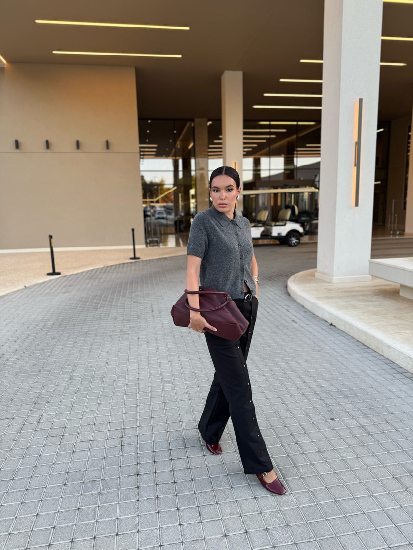 Stylishly dressed woman standing on a paved area with a building in the background wearing a bag