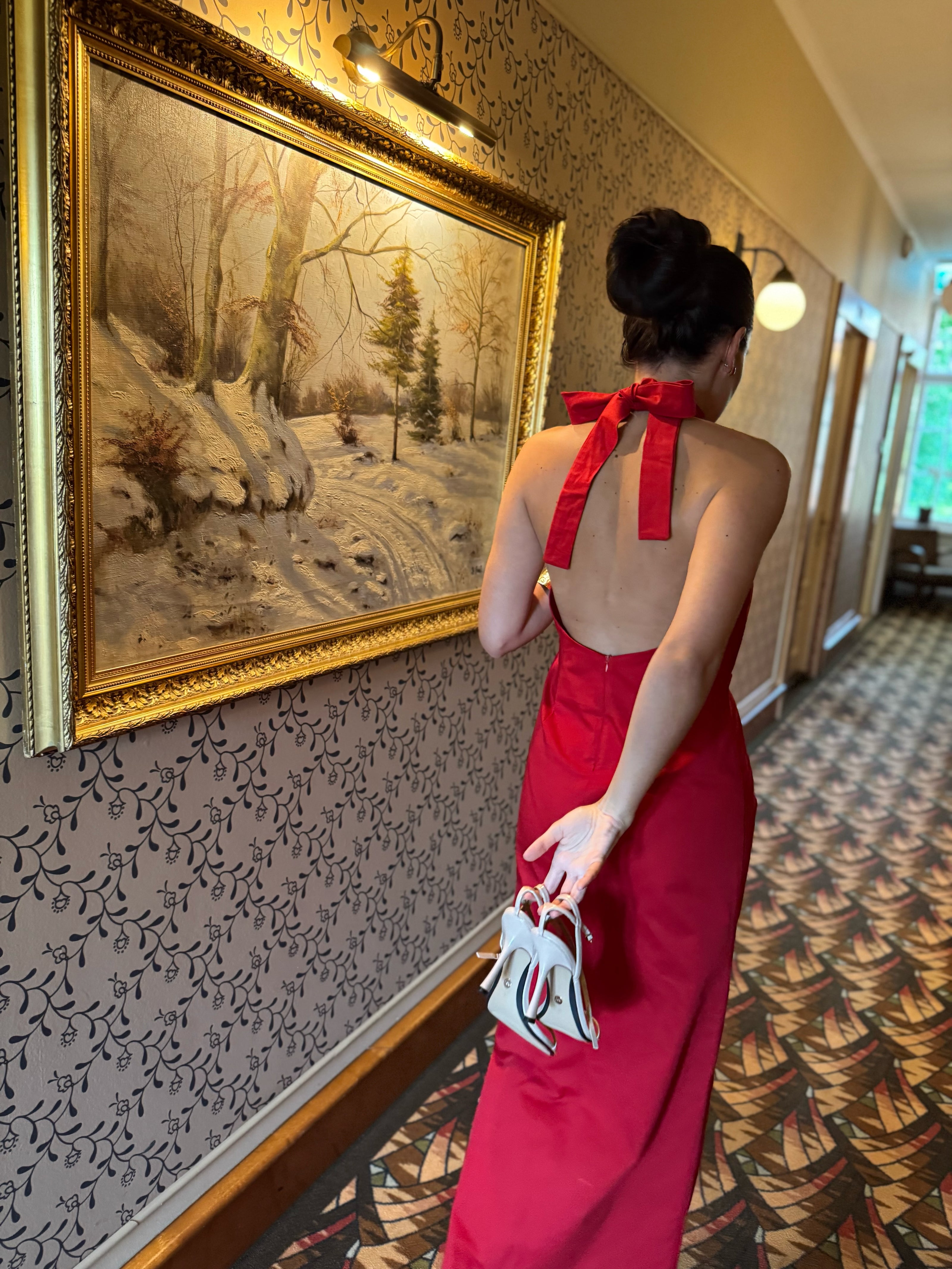 Woman in a red dress standing in a room with decorative wallpaper and a painting in Saaremaa.
