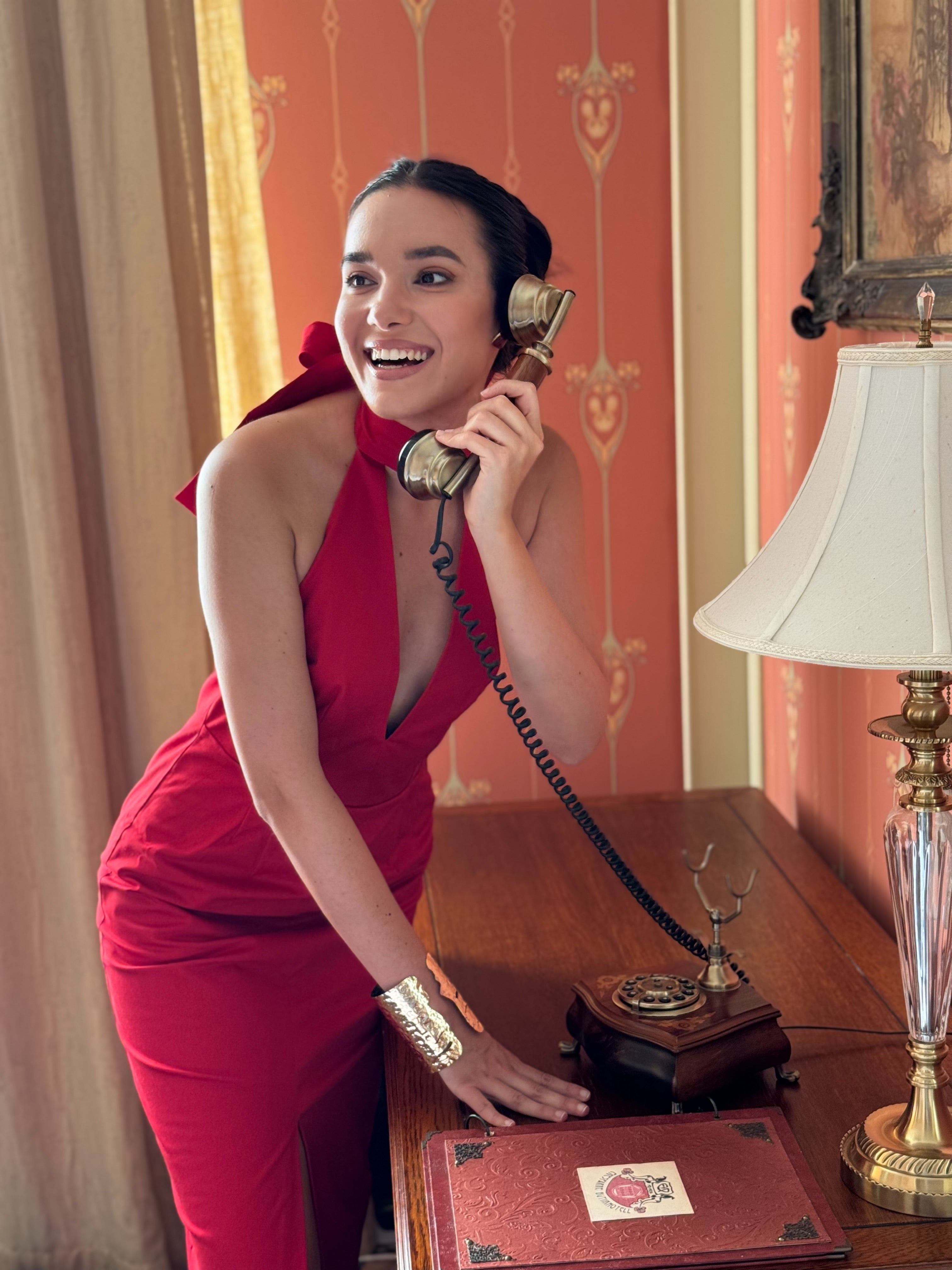 Woman in a red dress getting ready for New Year Party using a vintage telephone in an elegant room.