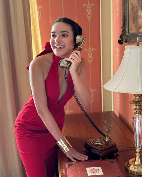 Woman in a red dress getting ready for New Year Party using a vintage telephone in an elegant room.