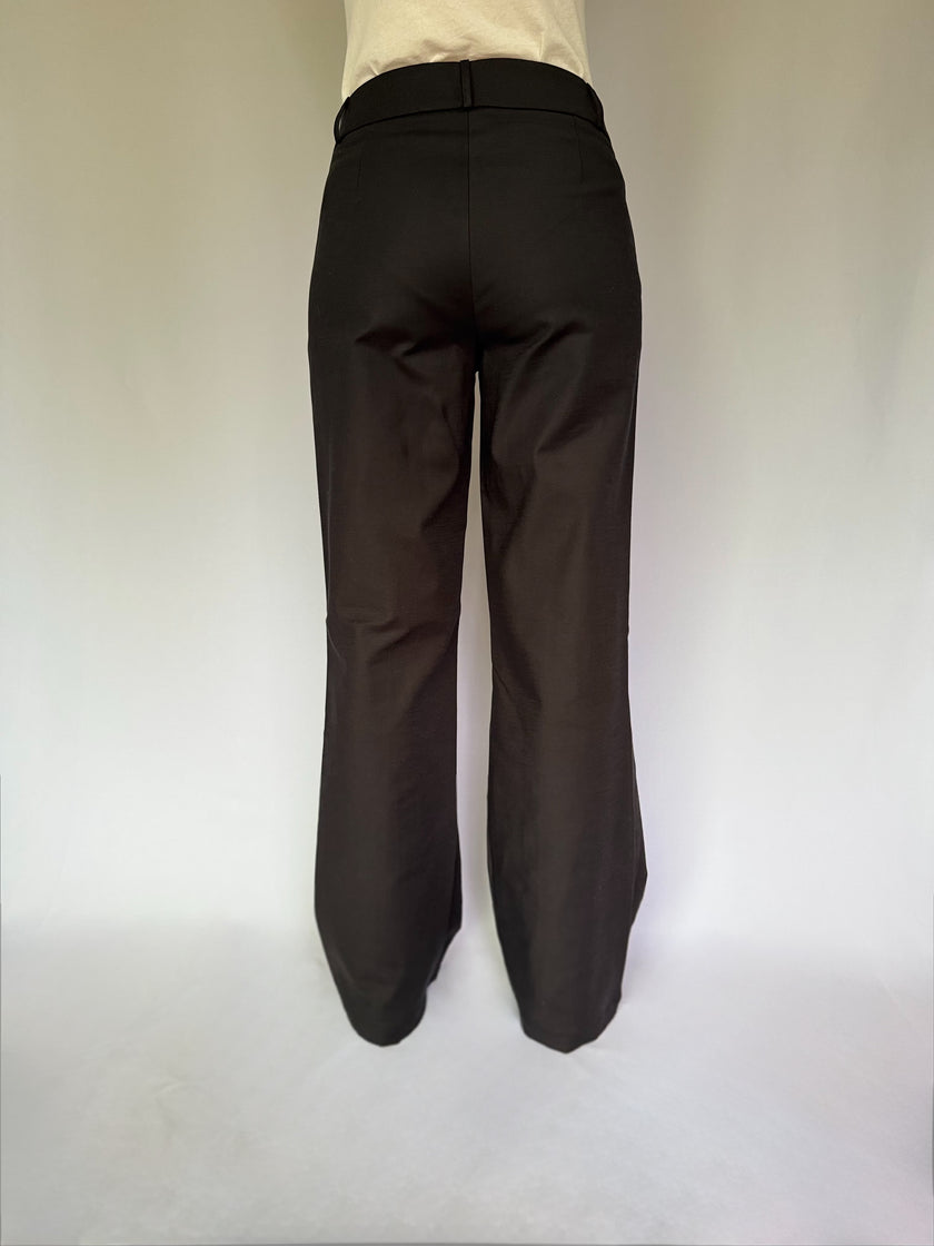 back view of a woman wearing baggy black dress pants on a white background