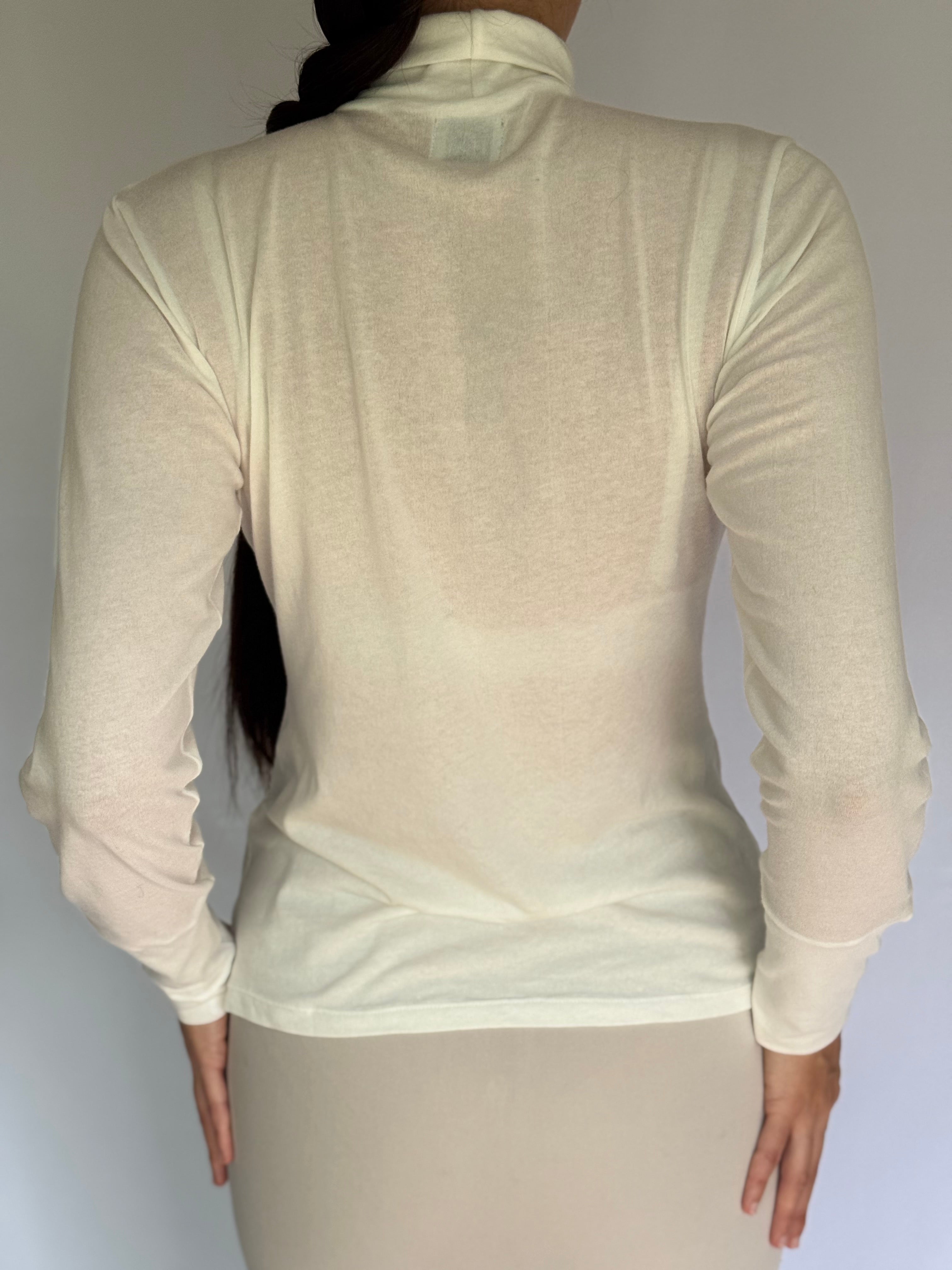 A young woman wearing an ivory long-sleeve top worn by a person on a plain background