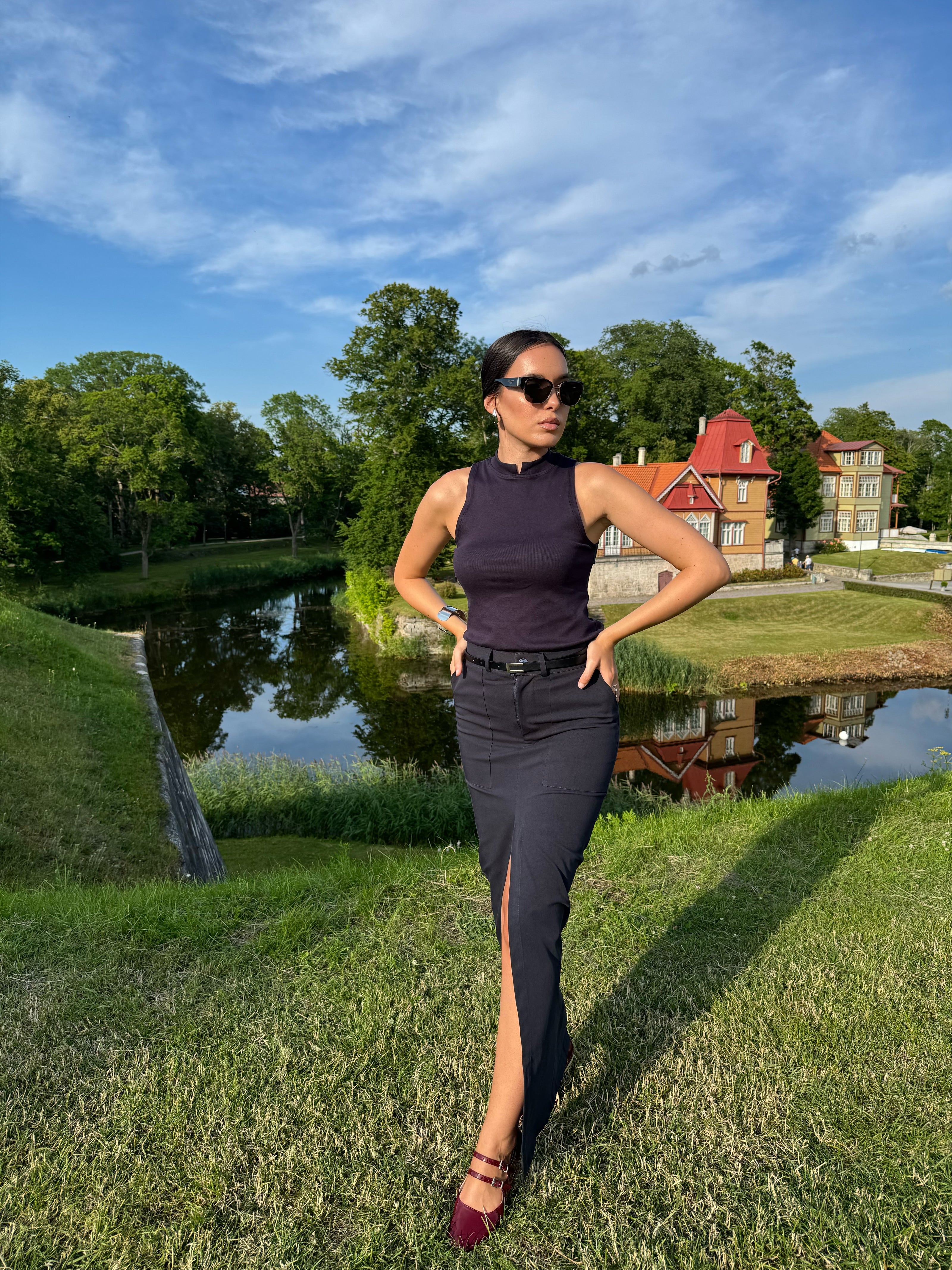 Woman in a black outfit standing in a park with a pond and trees in the background