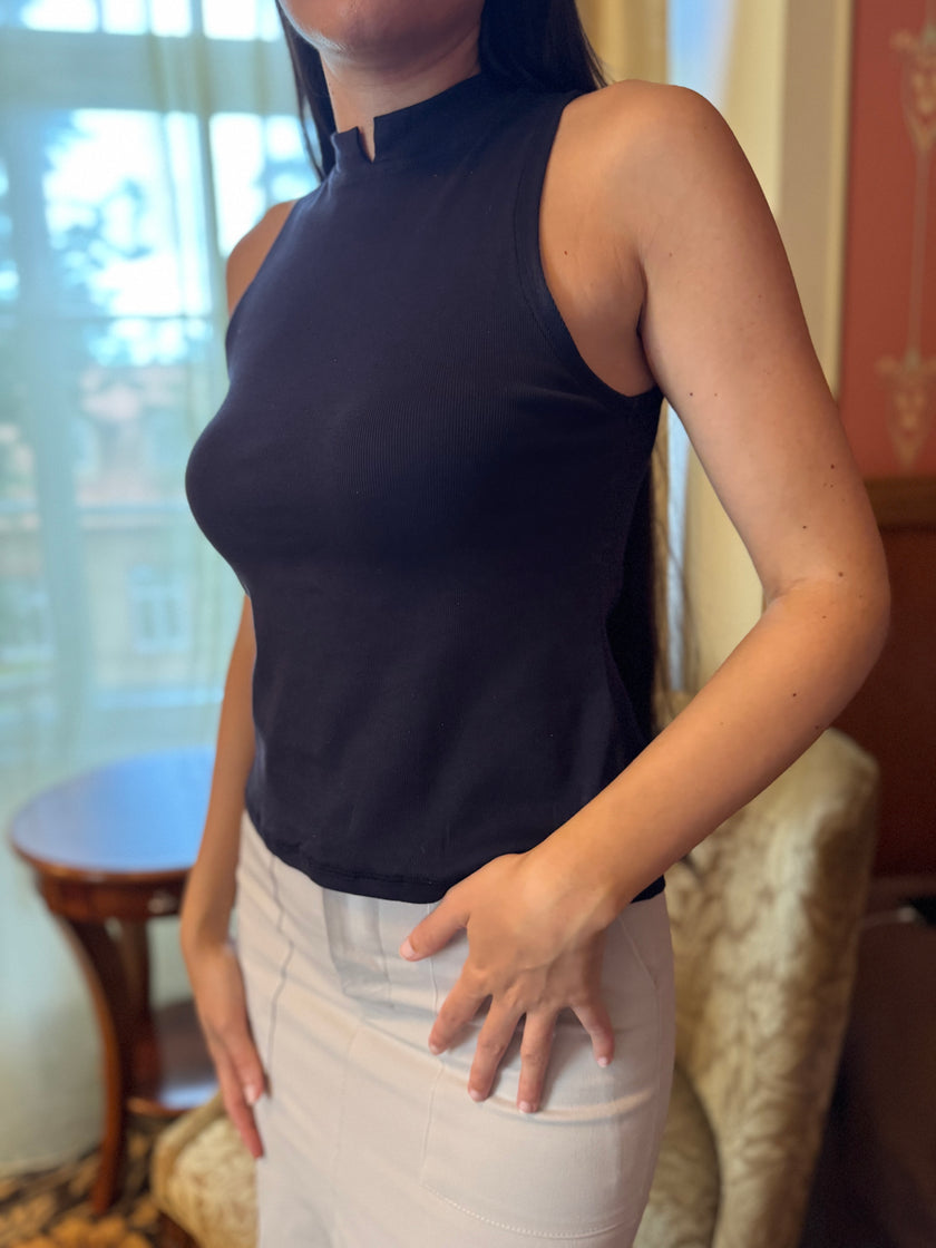 Person wearing a navy blue sleeveless top and white pants indoors.