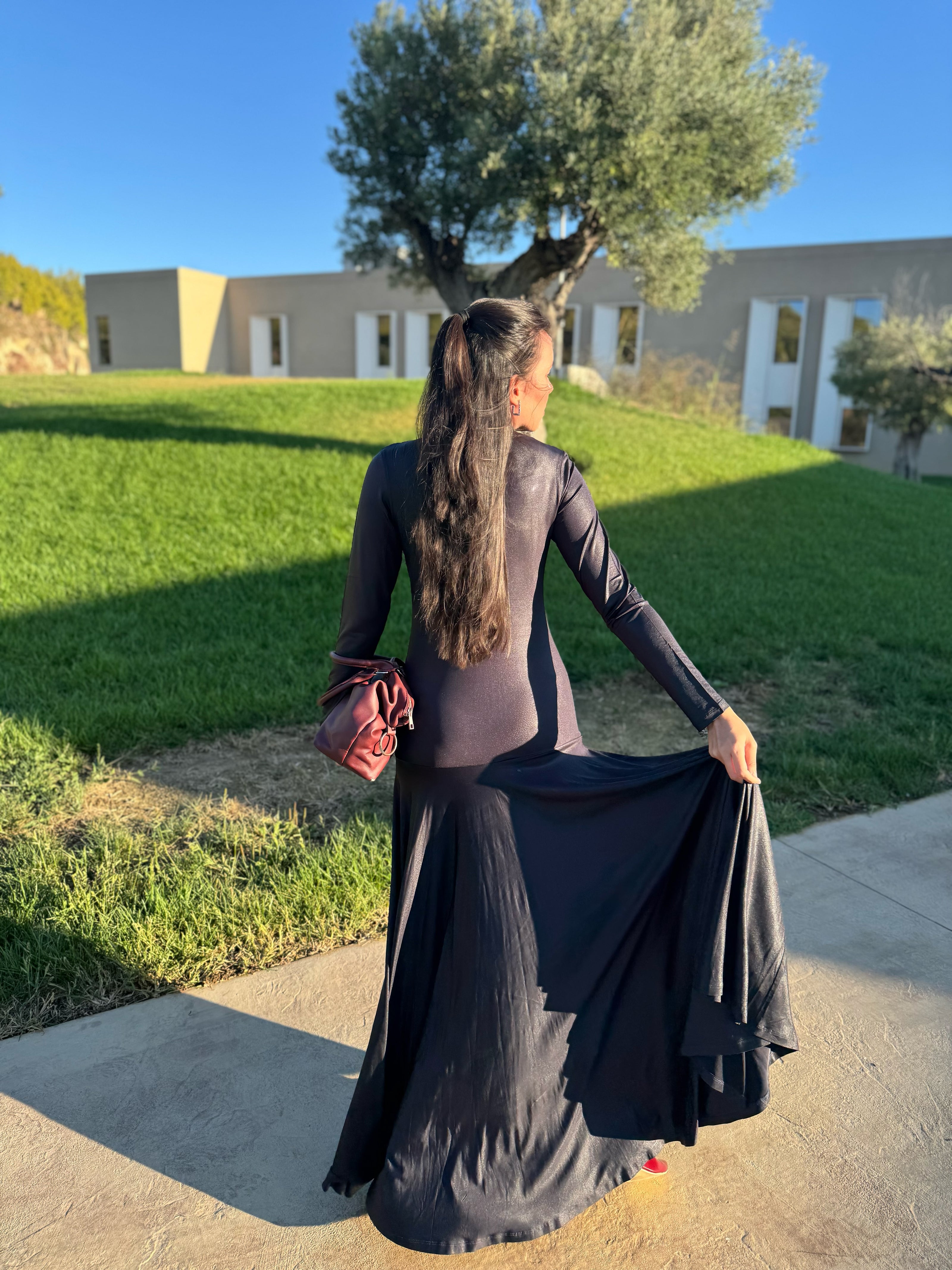 Person wearing a long black dress with a full circle skirt, standing outdoors on a sunny day.